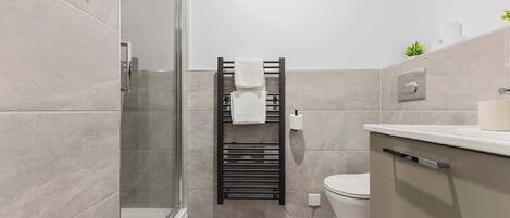 Une salle de bain moderne avec une douche à parois de verre, un porte-serviettes noir, des toilettes et un lavabo blanc.