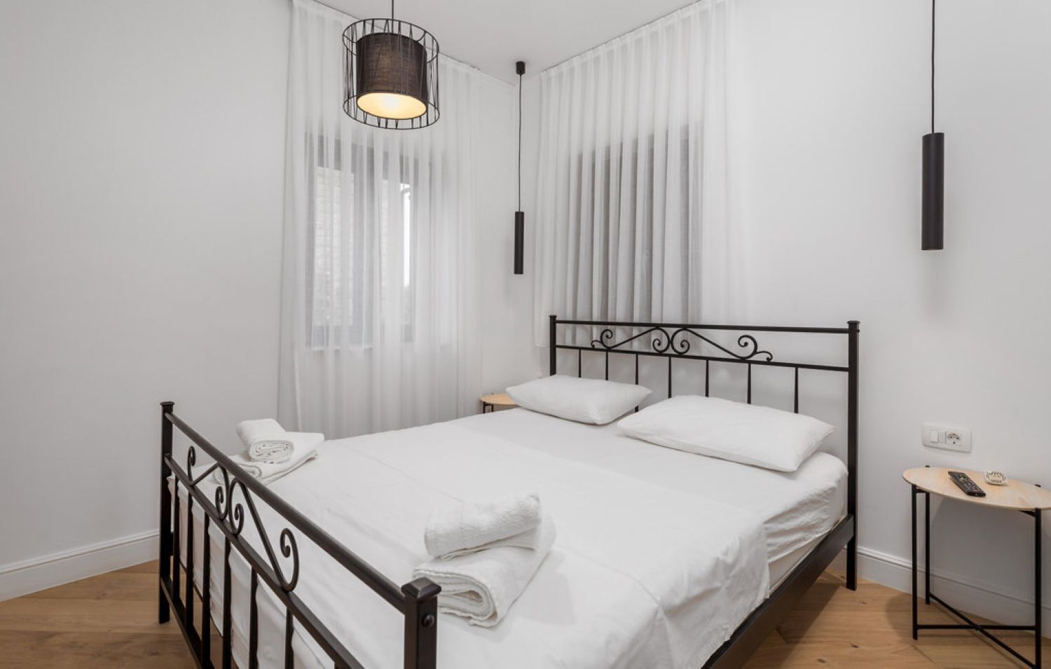 A modern bedroom with a metal bed frame, white bedding, and a hanging light fixture.