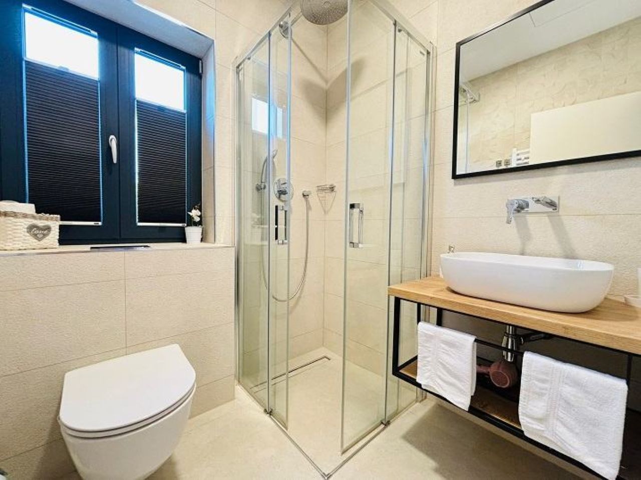 A modern bathroom with a glass-enclosed shower, a white toilet, a wooden vanity with a large white sink, and a mirror above the sink.