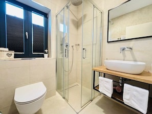 A modern bathroom with a glass-enclosed shower, a white toilet, a wooden vanity with a large white sink, and a mirror above the sink. - Villa Oblica (Jakišnica)