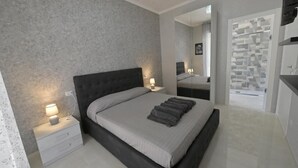 Een moderne slaapkamer met een groot bed, nachtkastjes met lampen, een spiegel en een badkamer met douche en toilet.