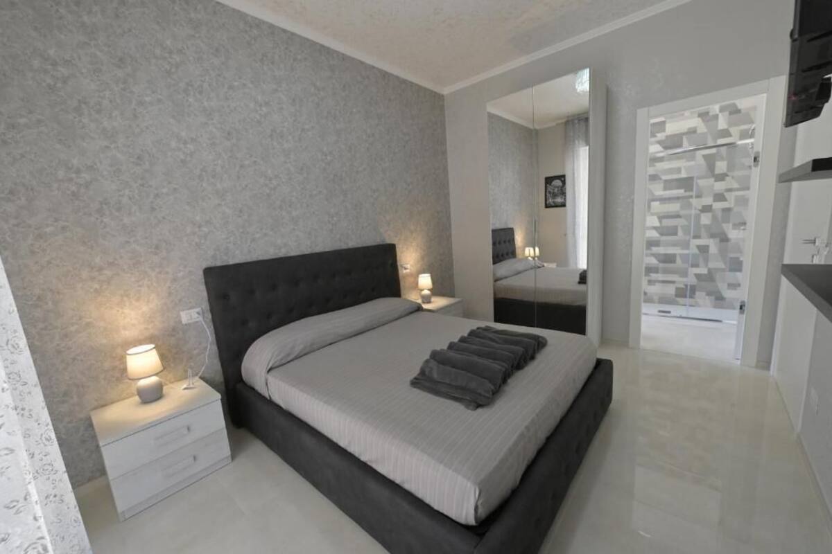 Une chambre moderne avec un grand lit, des tables de chevet avec des lampes, un miroir et une salle de bain avec une douche et des toilettes.