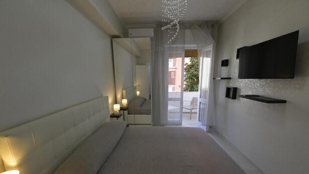 Een hotelkamer met een groot bed, een aan de muur bevestigde televisie, een nachtkastje met lamp en uitzicht op het balkon.