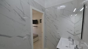 Een moderne badkamer met marmeren wanden, een witte wastafel en een spiegel.