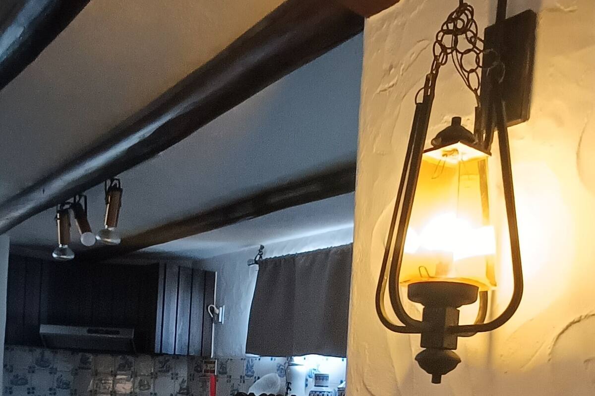 Une cuisine avec un luminaire suspendu, un plafond avec poutres apparentes et un mur recouvert de carreaux.