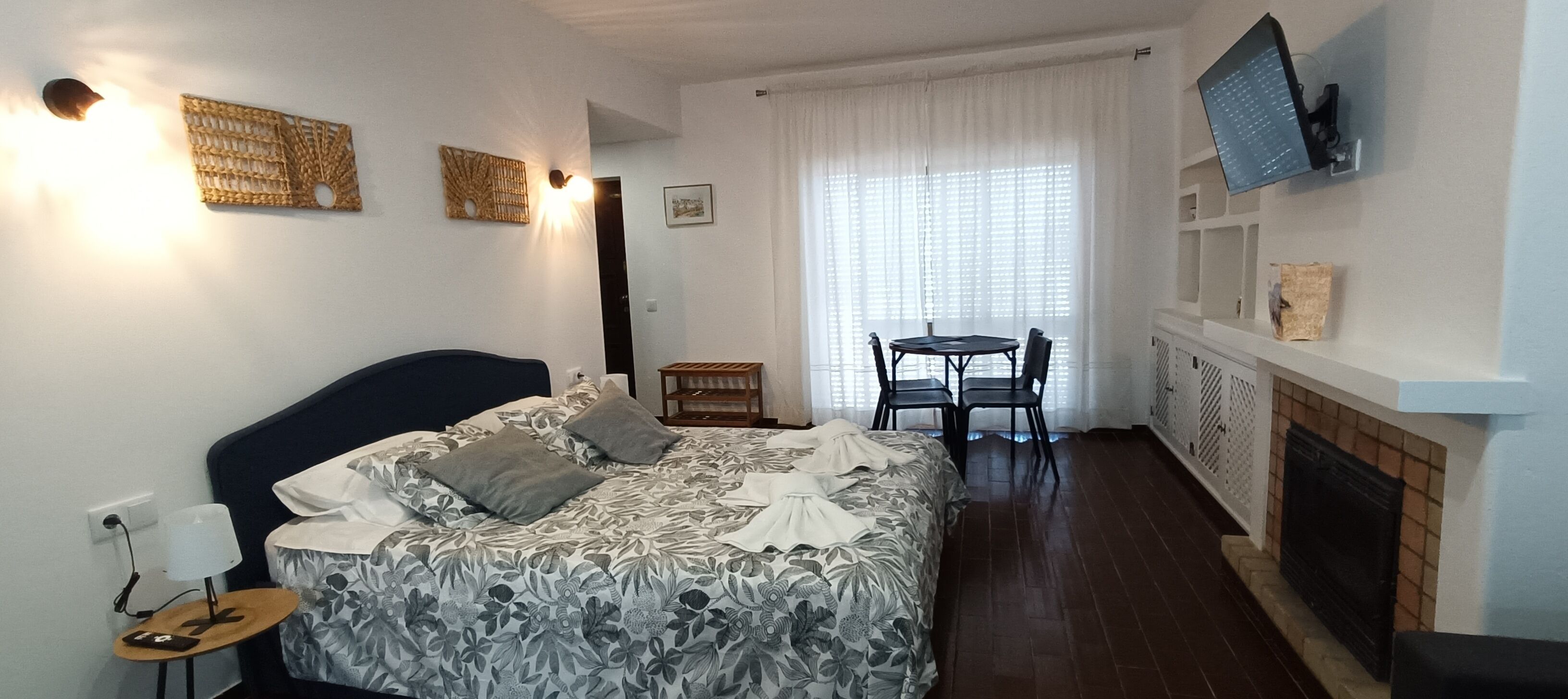 Un dormitorio con cama, mesita de noche, lámpara y televisor montado en la pared.