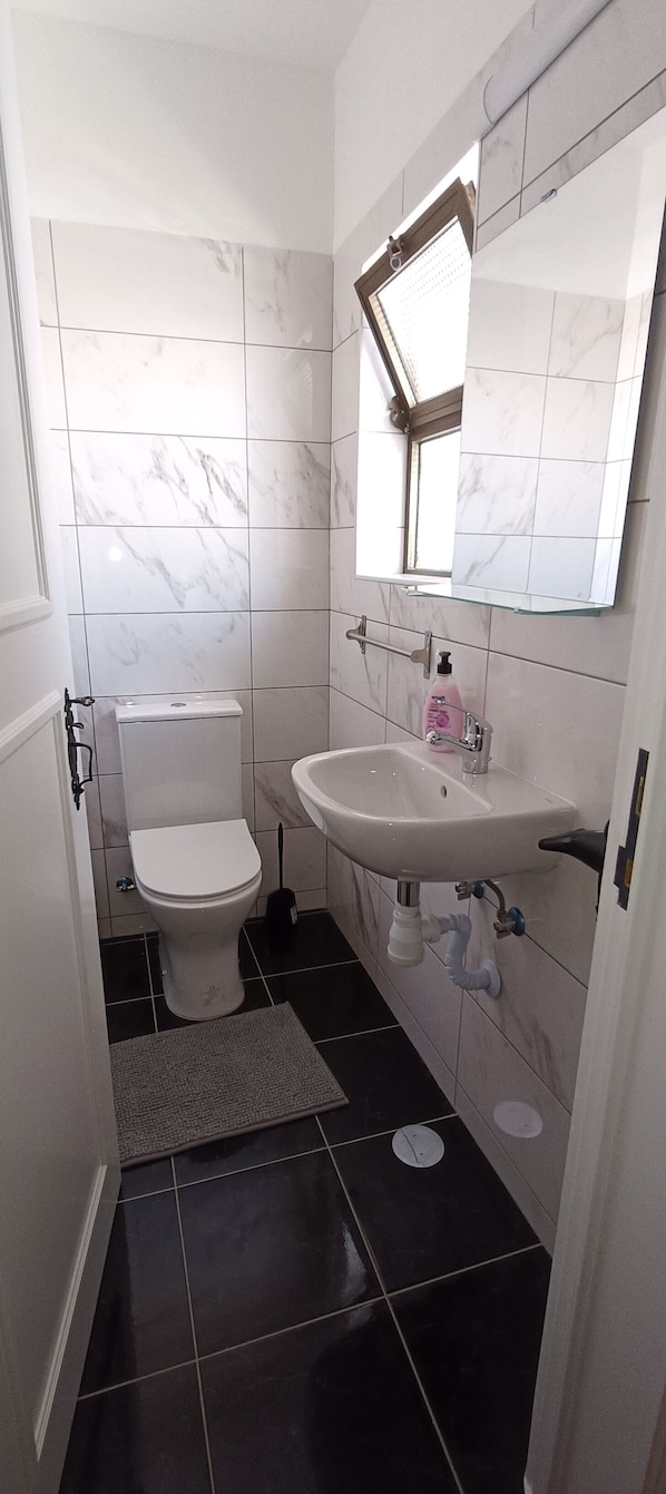 A bathroom with a toilet, sink, mirror, and tiled walls. - Villa Golden Coast -Lagos (Lagos)