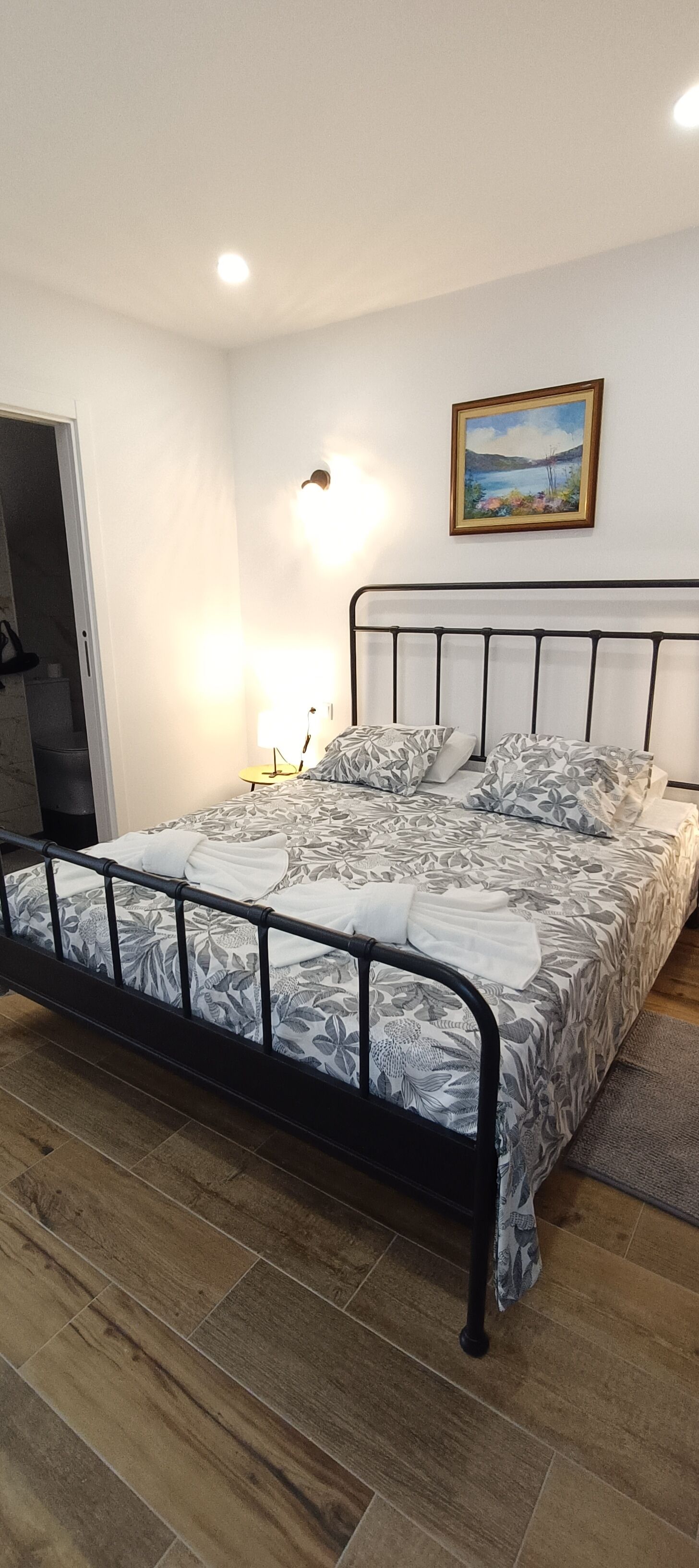 Un dormitorio con una cama, un cuadro y una mesita de noche.