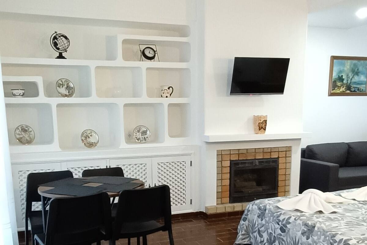 Une pièce avec un sol en briques, une table à manger avec des chaises, un canapé, un téléviseur fixé au mur et une cheminée.