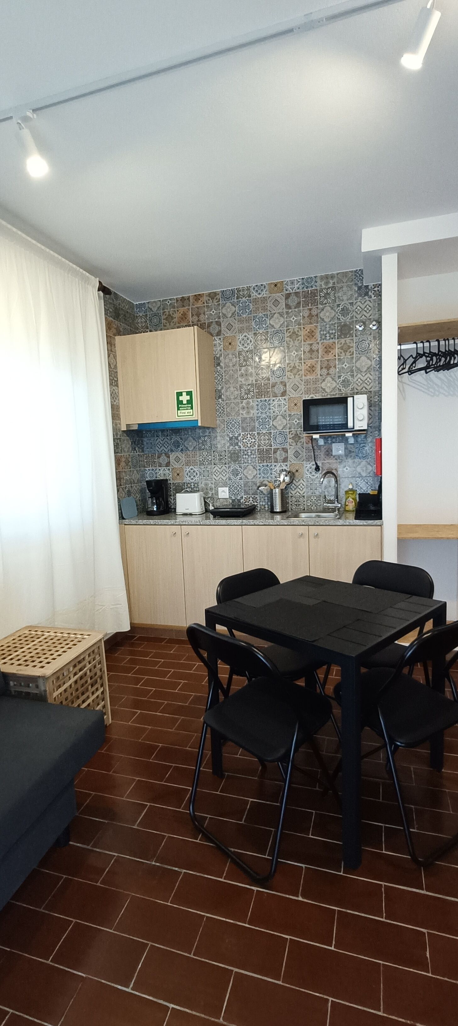 A compact kitchen with a microwave, toaster, and coffee maker. There is a table with chairs, a cabinet, and a patterned backsplash.
