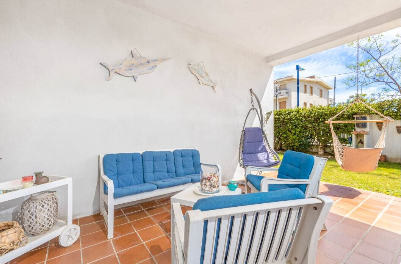 Un espace patio avec une table blanche, des chaises bleues et un canapé blanc. On peut voir des poissons décoratifs sur le mur et une chaise suspendue.