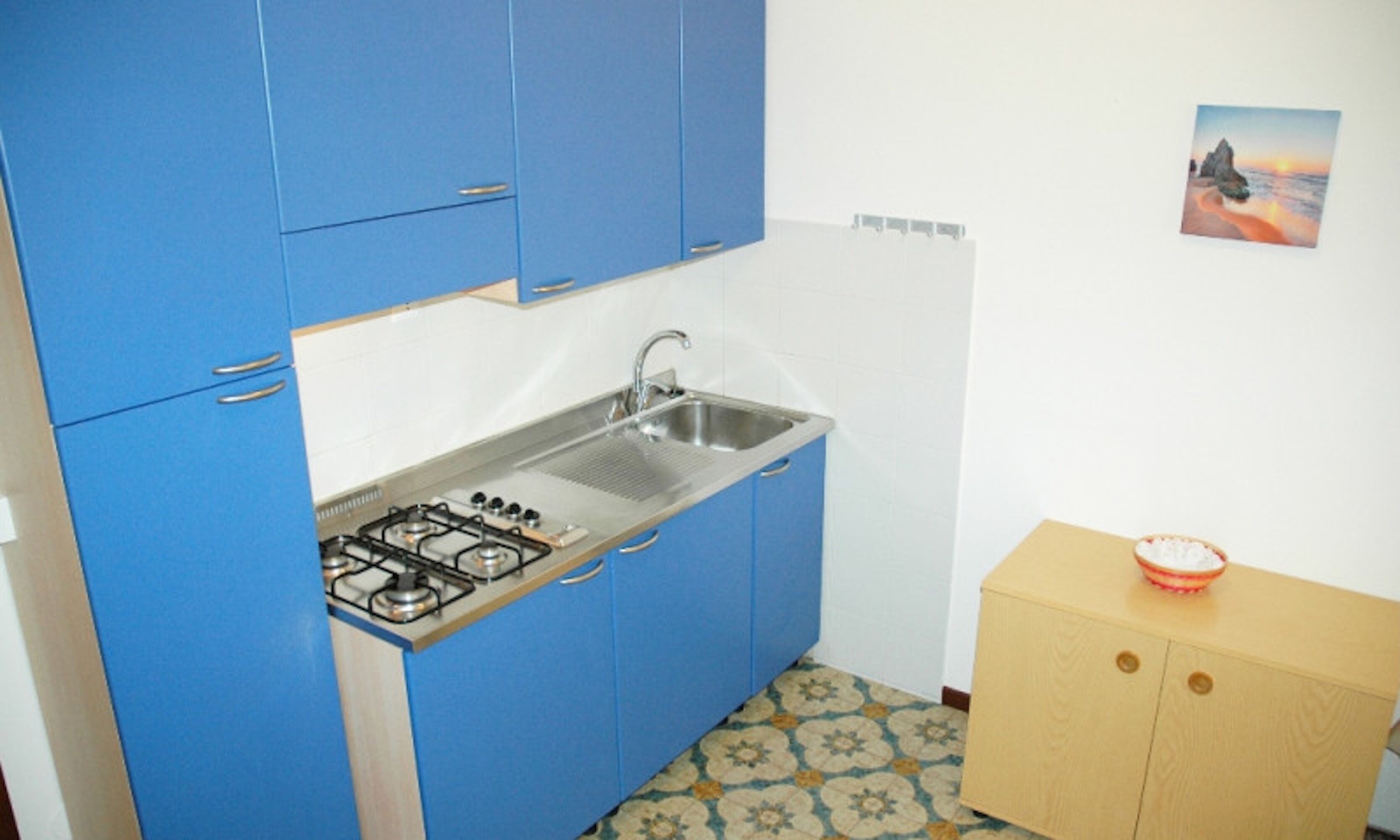 A compact kitchen with blue cabinets, a stainless steel sink, and a gas stove.
