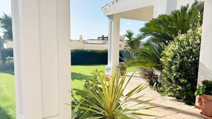 A covered patio area with a potted plant, a white column, and a view of a well-maintained lawn and house in the background. - Elegant Private Villa with Pool & Scenic View (Mijas)