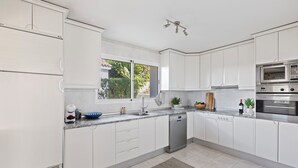 A modern kitchen with white cabinetry, a built-in dishwasher, a microwave, and a large window providing natural light. - Elegant Private Villa with Pool & Scenic View (Mijas)