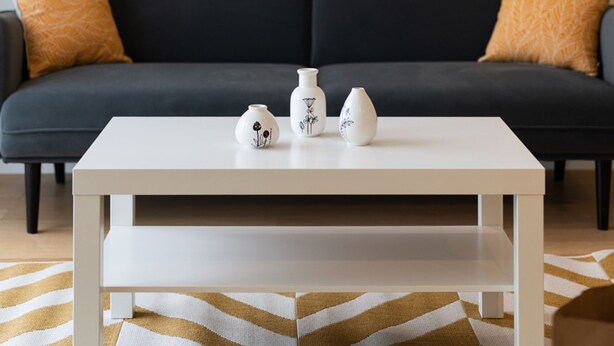 A modern living room with a dark grey sofa, two matching orange pillows, and a white coffee table with two white vases. - LIV - Comfortable Athens Studio S8-2c (Athens)