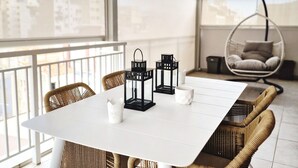 En moderne balkon med et hvidt bord, fletstole, sorte lanterner og en hængekøjsstol.
