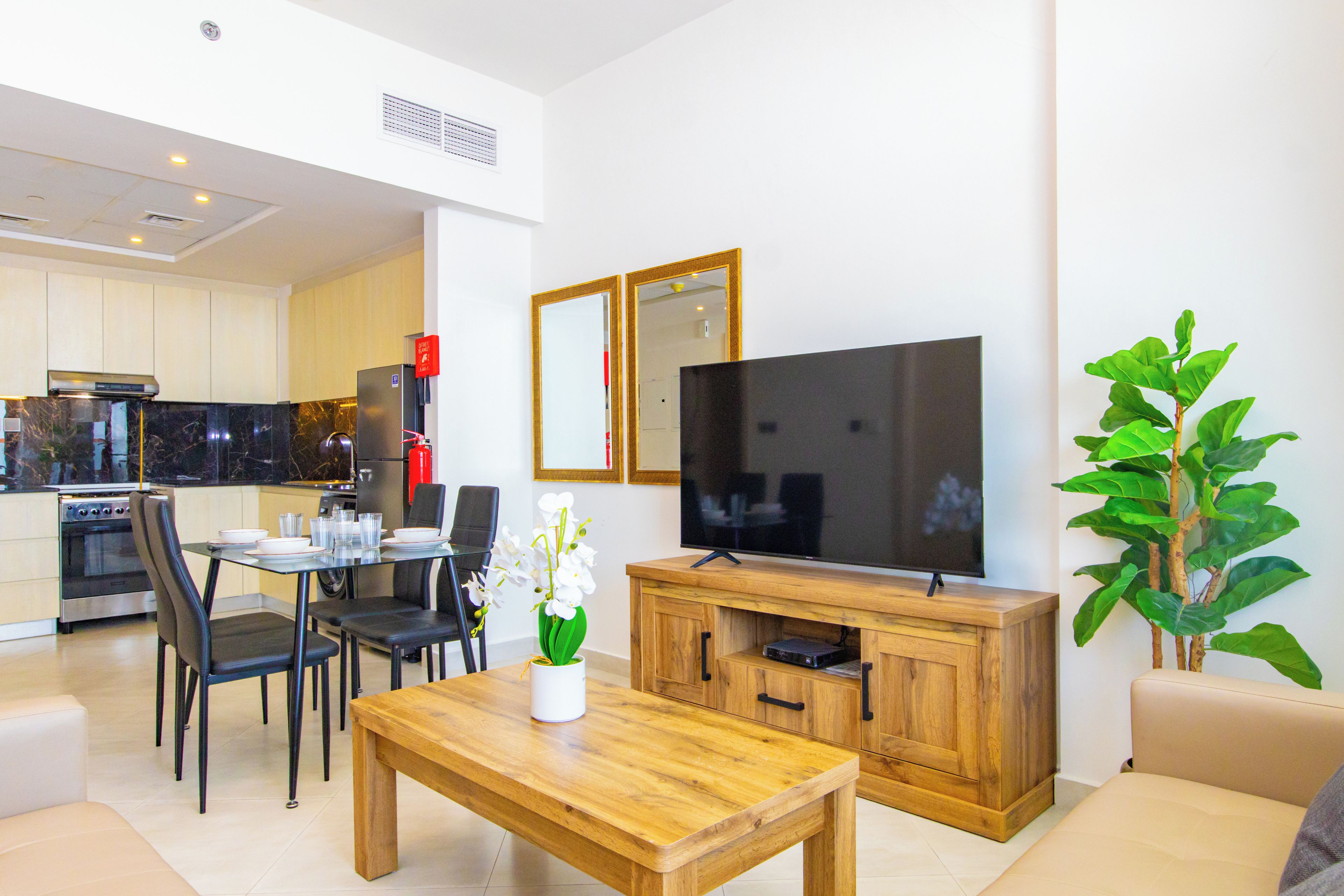 A modern living room with a flat-screen TV, wooden coffee table, and a dining area with chairs and a table.