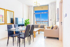 A modern living room with a dining area, a sofa, a coffee table, and a television. - Bloomfields 1BR - Binghatti Avenue - Jaddaf (Dubai)