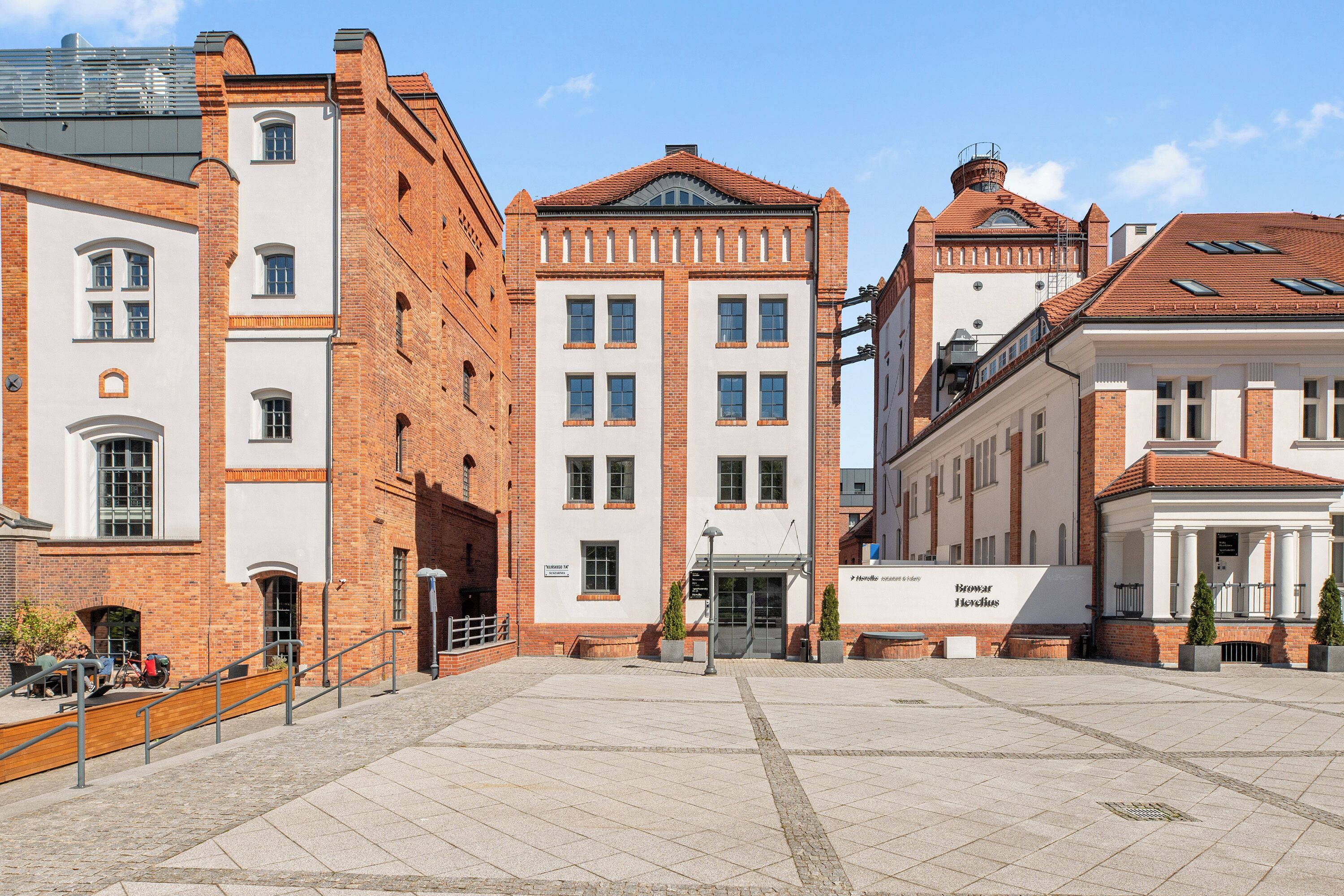 A spacious public square with a central building featuring a classical architectural style, surrounded by other buildings with brick facades.