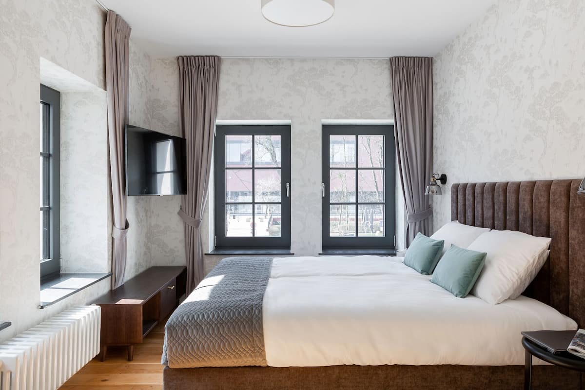 Un dormitorio moderno con una cama grande, televisión y dos ventanas con cortinas.