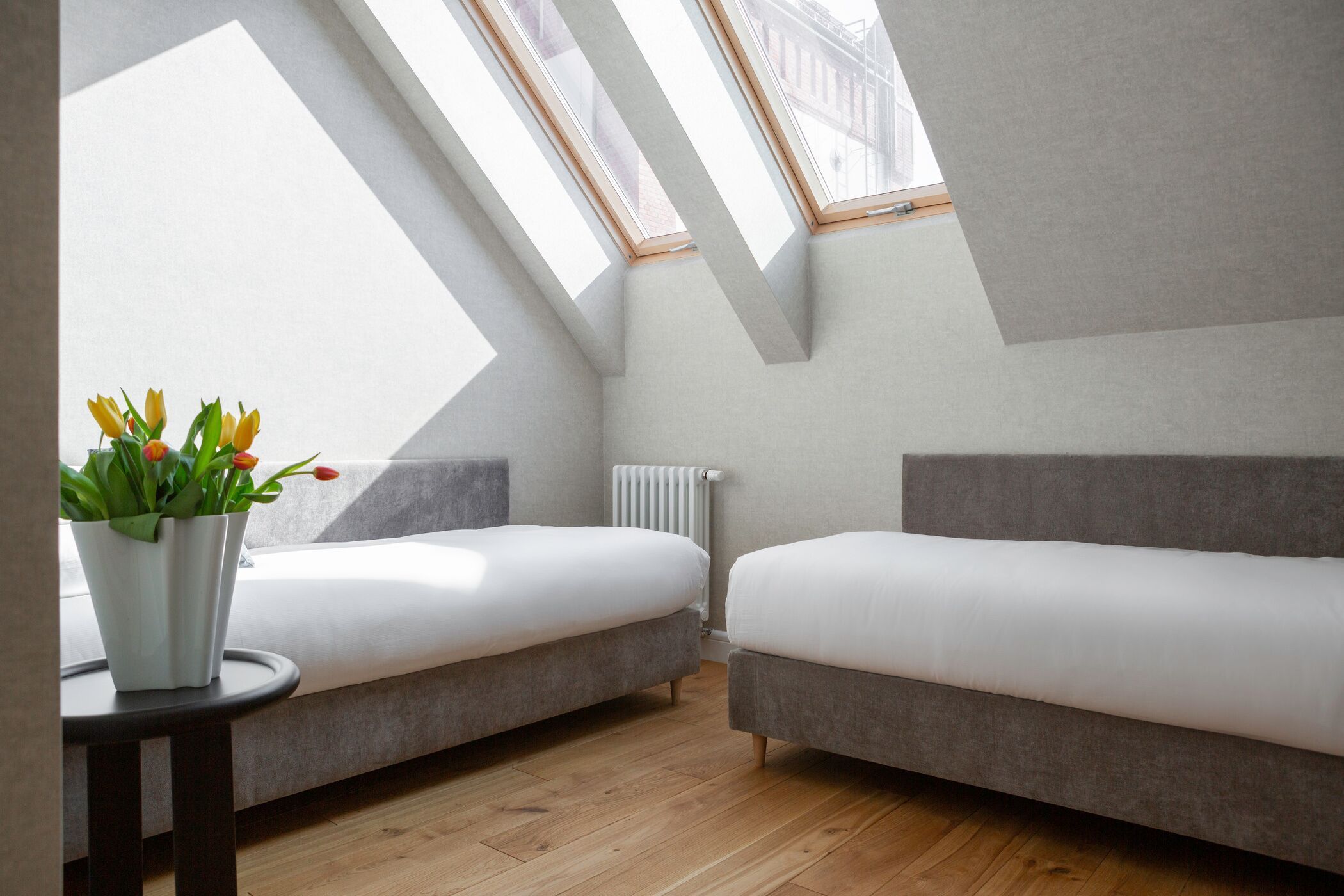 Une chambre de style loft moderne, dotée d’une lucarne, de deux canapés gris, d’une table ronde en bois et d’une plante en pot.