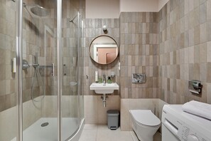 Un baño moderno con ducha envuelta en vidrio, espejo redondo, lavamanos y retrete.
