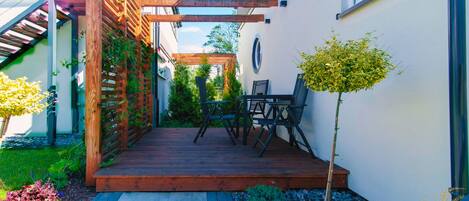 A wooden deck with a pergola, a small table and chairs, and a potted plant.
