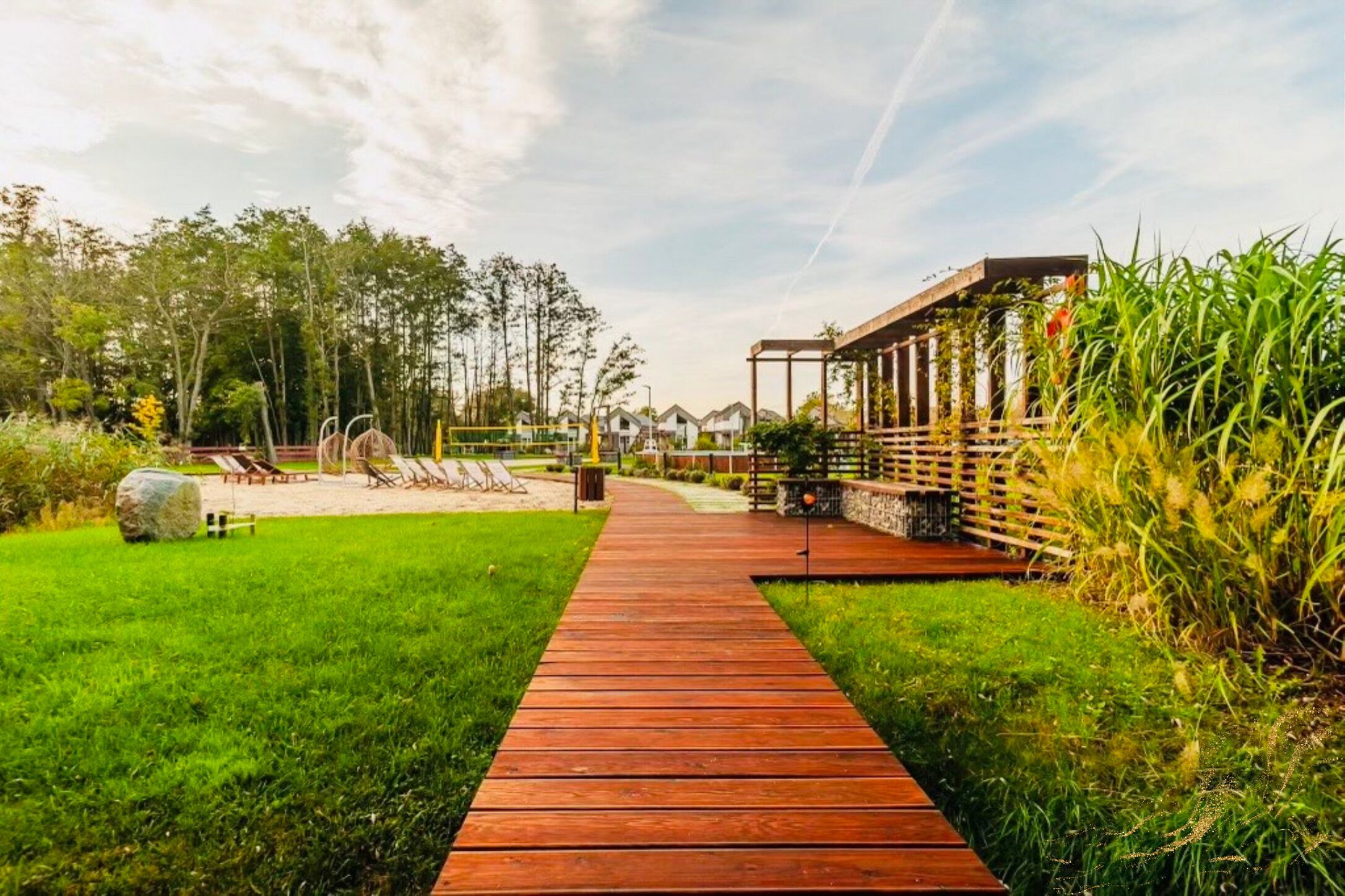 A wooden pathway leading to a covered outdoor area with lounge chairs and a stone wall.