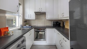 A compact kitchen with white cabinets, a stainless steel oven, a microwave, and a washing machine. - Tranquil 1-bedroom apartment in beautiful Knysna perfect for relaxing (Knysna)
