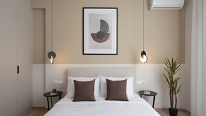 A modern hotel room with a large bed, two bedside tables, a framed artwork, an air conditioner, and a potted plant. - Luxury & Spacious Penthouse in Athens with Terrace  (Athens)