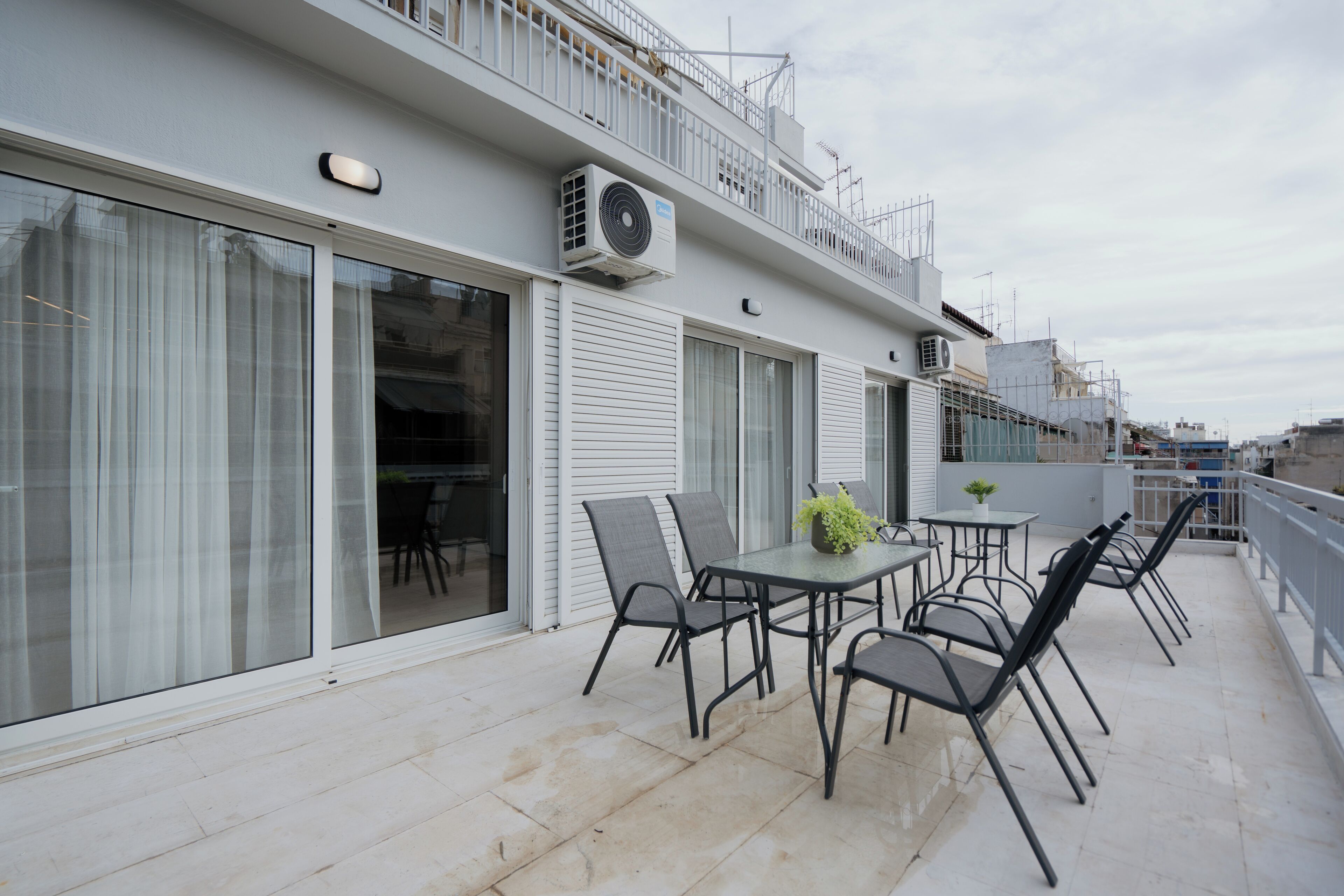 An outdoor patio with a table and chairs, a potted plant, and a white railing.