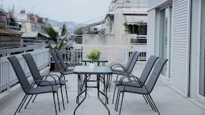 A balcony with a table and chairs, a potted plant, and a view of buildings and mountains in the background. - Luxury & Spacious Penthouse in Athens with Terrace  (Athens)