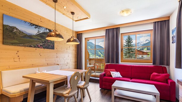 En inredning med träpanel, ett matbord, stolar, en röd soffa och ett stort fönster med utsikt över bergen.