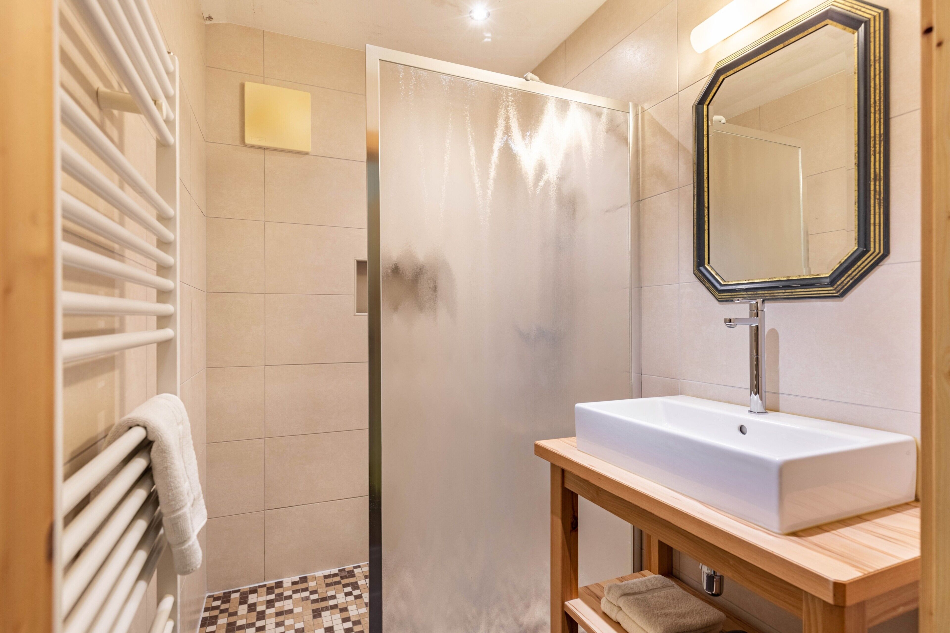 Een badkamer met een douche, wastafel, spiegel en handdoekhouder.