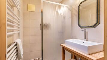 Een badkamer met een douche, wastafel, spiegel en handdoekhouder.