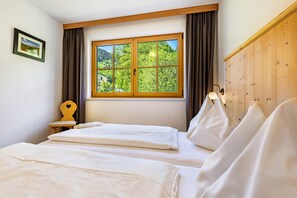 Une chambre avec deux lits, une fenêtre donnant sur un paysage verdoyant, une tête de lit en bois et une petite table de chevet.