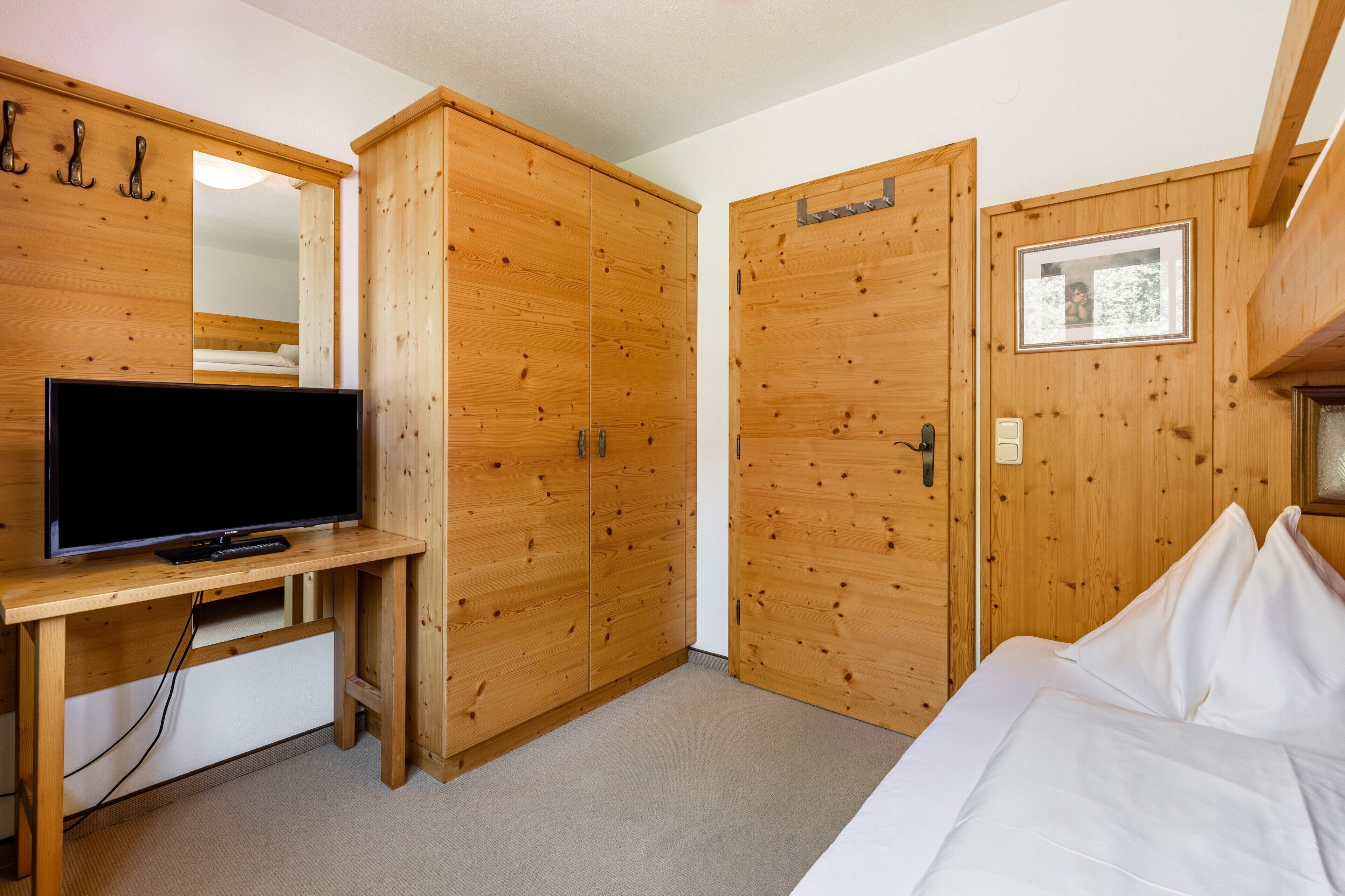Ein Schlafzimmer mit einem Holzkoffer, einem Bett, einem Fernseher auf einem Holzschrank und einem Spiegel an der Wand.