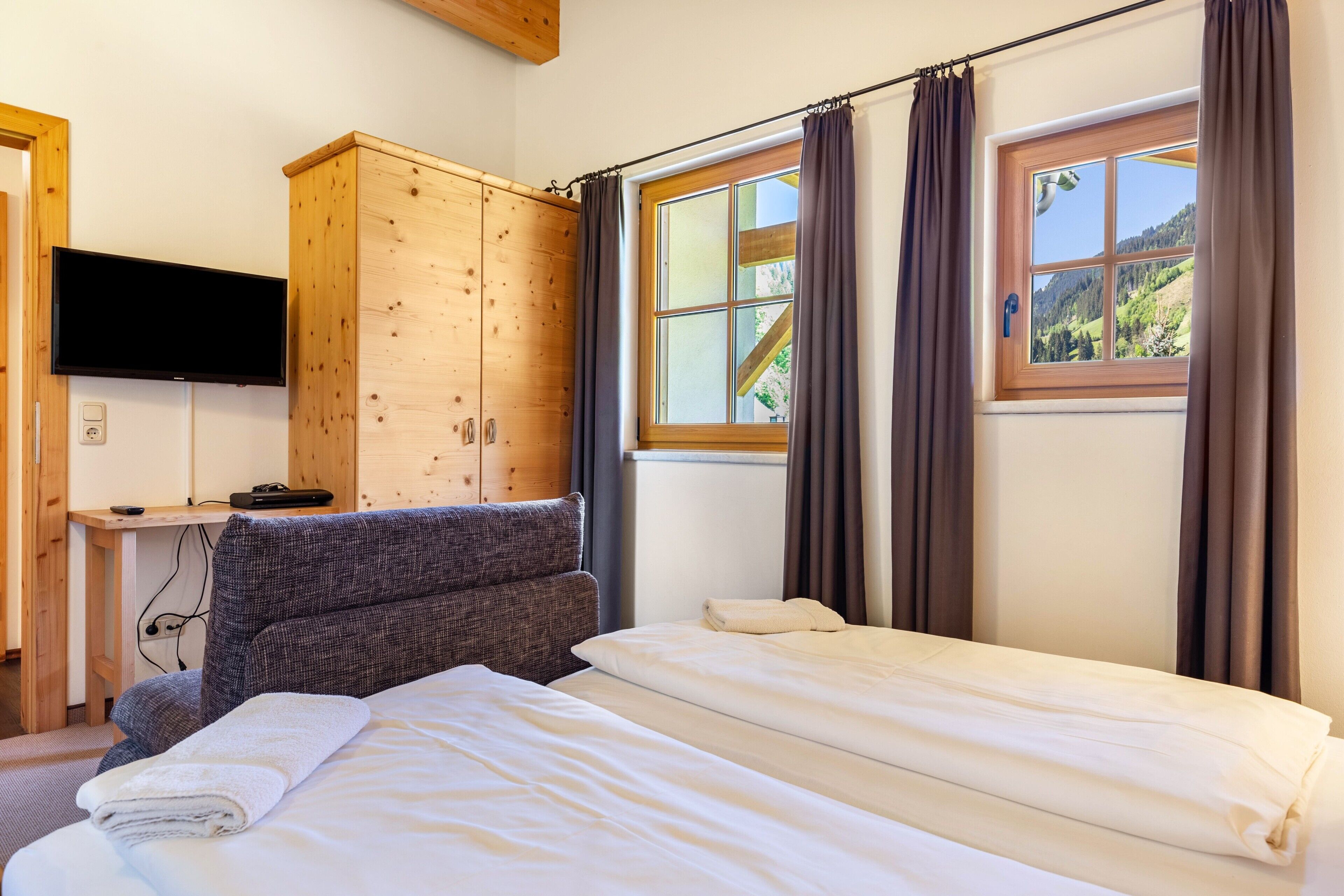 Een slaapkamer met een bed, een houten kledingkast, een televisie en een raam met gordijnen.