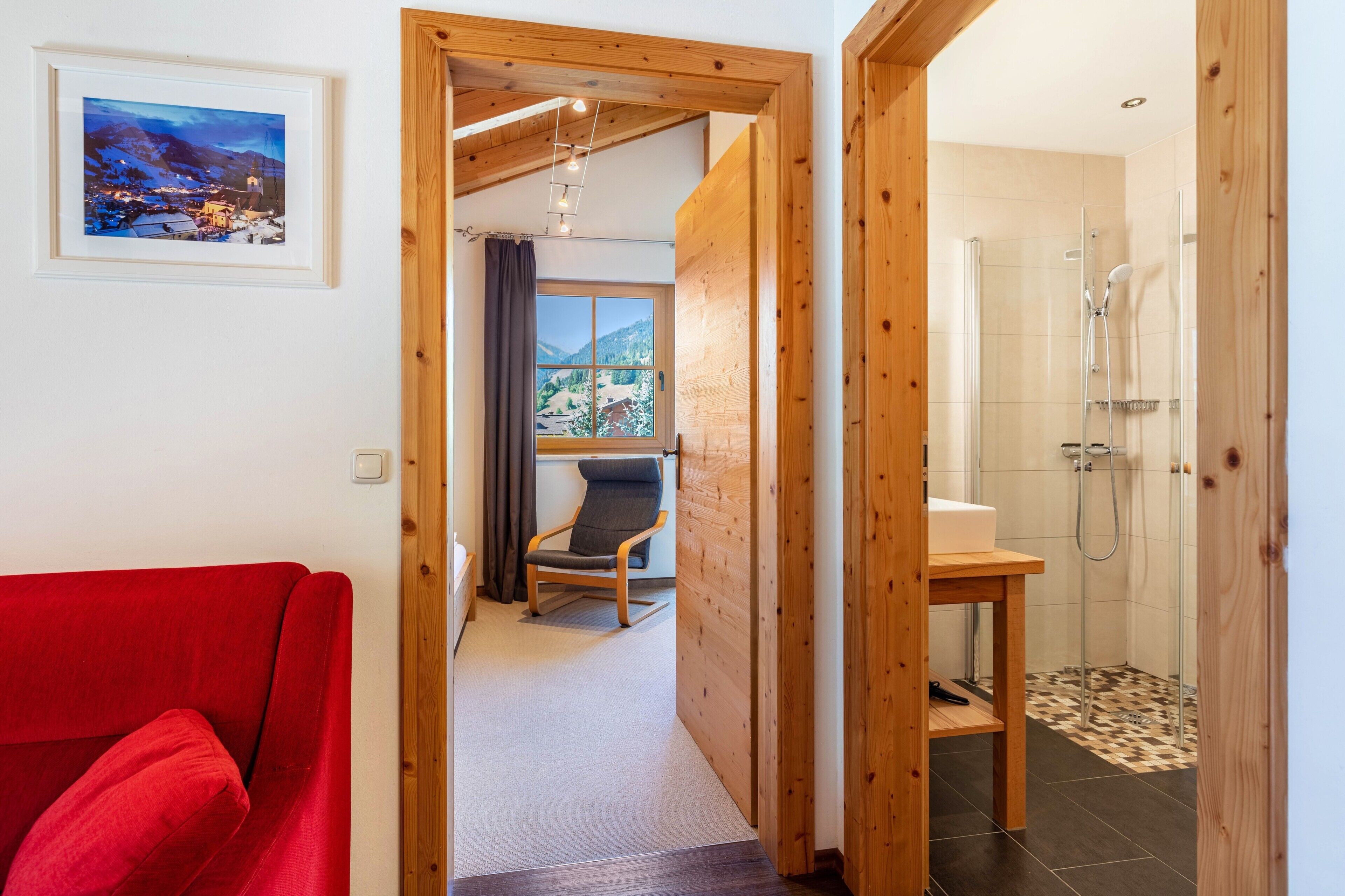A wooden interior with a red sofa, a framed picture, a chair, and a shower area.