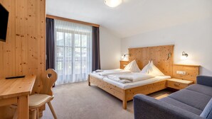A hotel room with a wooden bed, a desk, a chair, a sofa, and a window with curtains. - Apartment 'Stockinger B4' with Mountain View, Shared Garden and Wi-Fi (Unterberg)