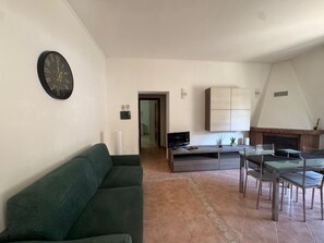 Un soggiorno moderno con un divano verde, un'area pranzo con tavolo e sedie, un camino e un angolo cucina con pensili.