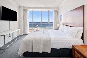Habitación de hotel con una cama grande, televisión de pantalla plana, mesita de noche y vista al océano.