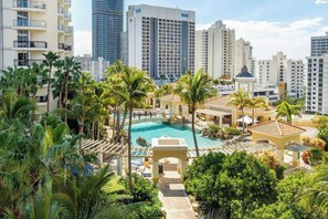 Un hotel con piscina rodeado de palmeras y un paisaje urbano al fondo.