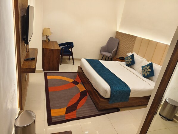 A hotel room with a bed, desk, chair, and a TV mounted on the wall. - The Venue By SK (Greater Noida)