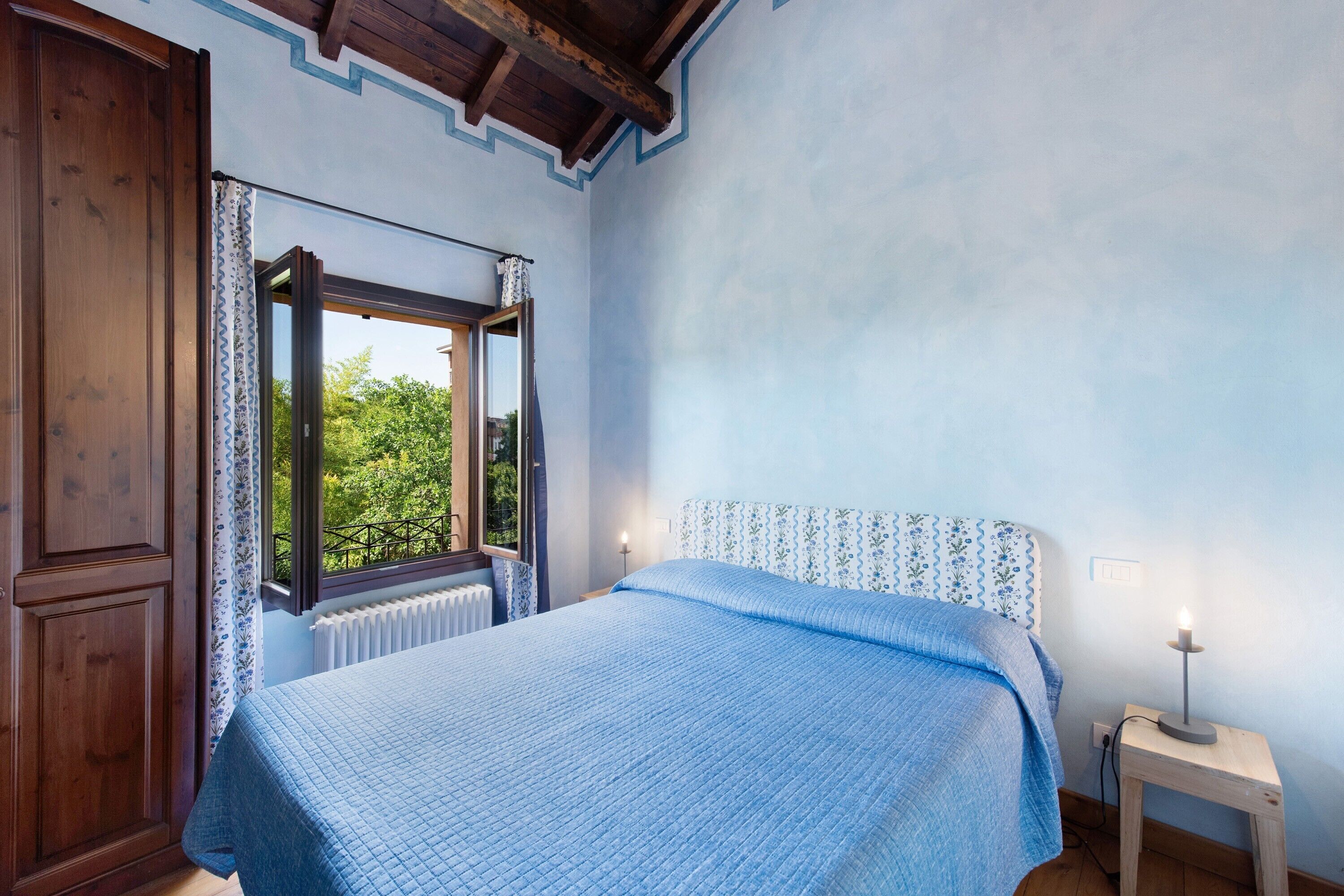 Une chambre à coucher avec un lit, une fenêtre, un radiateur et une table de chevet avec une lampe.