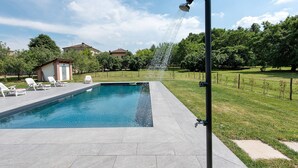 A swimming pool with a water feature, surrounded by a grassy area and trees. - Cascine di Villa Schella with Pool – Relaxing Oasis for Groups and Families (Ovada)
