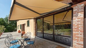 A patio with a table and chairs, a large window, and a brick wall. - Cascine di Villa Schella with Pool – Relaxing Oasis for Groups and Families (Ovada)