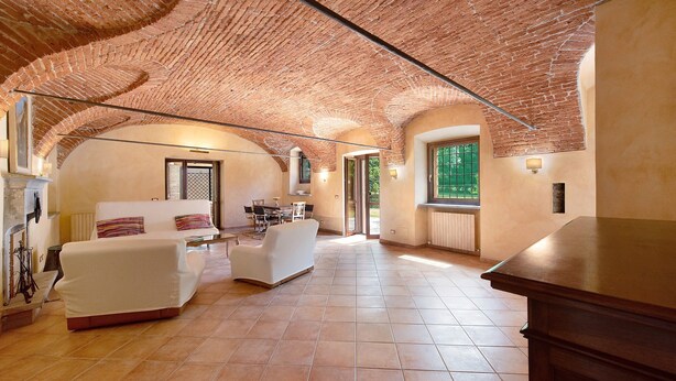 A spacious room with a brick ceiling, a white sofa, a dining table, and a window with a view. - Cascine di Villa Schella with Pool – Relaxing Oasis for Groups and Families (Ovada)