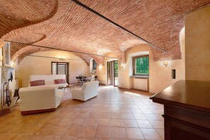 A spacious room with a brick ceiling, a white sofa, a dining table, and a window with a view. - Cascine di Villa Schella with Pool – Relaxing Oasis for Groups and Families (Ovada)