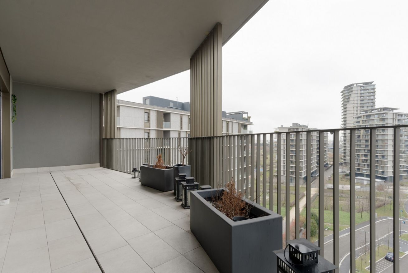 Ein Balkon mit Blick auf umliegende Gebäude, einem Kachelboden und rechteckigen Pflanzgefäßen mit Pflanzen.